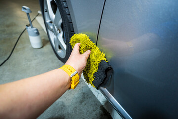 Close-up of a worker's hand washing the side of a car with a yellow hand wash. Cleaning a car in a garage.