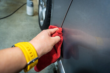 Close-up of a worker's hand washing the side of a car with a red hand wash. Cleaning a car in a garage.