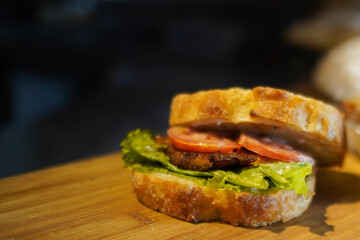 Close-up of a homemade artisan sandwich with fresh lettuce, tomato, and grilled patty on rustic bread. Warm lighting, shallow depth of field, perfect for food ads, menus, blogs, and commercial use.