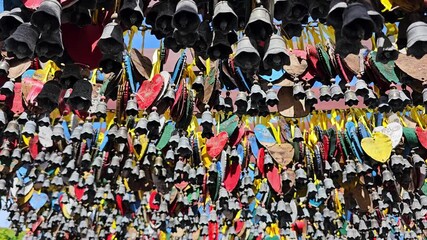 Colorful prayer wishes and bells at Nanshan Temple in Sanya. Heart-shaped tags with Chinese calligraphy, yellow ribbons and small bells. Traditional Buddhist blessing wall with vibrant colors.
