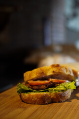 Vertical close-up of an artisan sandwich with lettuce, tomato, and grilled patty on rustic bread. Warm lighting and shallow depth of field, perfect for menus, blogs, ads, and food marketing.