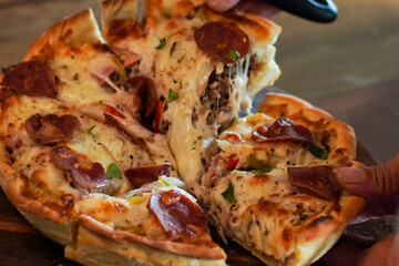 Vertical close-up of a hand lifting a hot pizza slice with melted cheese pull and savory toppings. Warm natural lighting and shallow depth of field ideal for menus, ads, blogs, and food marketing