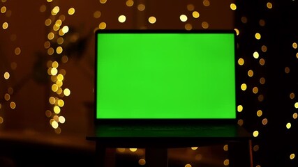 Man sitting with laptop, green screen display for replacement, working or browsing at home at dark background. Male person using computer indoors, mockup screen for app or website design.