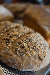 Close-up of fresh artisan multigrain bread topped with seeds and grains, displayed on a rustic bakery tray. Textured crust, organic ingredients, perfect for bakery, food, and culinary themes