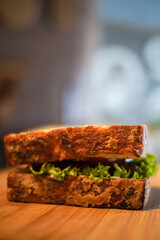 Close-up of a rustic artisan sandwich made with crusty toasted bread and fresh green lettuce on a wooden board. Warm, natural light and shallow depth of field create a gourmet, café-style look.