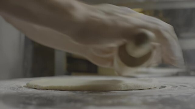 Hands rolling dough with a wooden pin on a flour-dusted surface