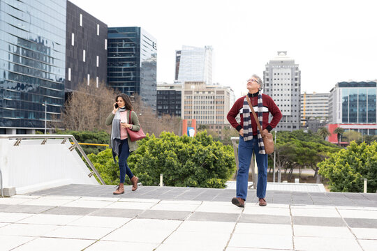 Diverse pedestrians standing and walking on plaza carrying bags, holding coffee cup and smartphone