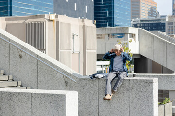 Asian man sitting on rooftop terrace wearing headphones, backpack and travel coffee cup, copy space
