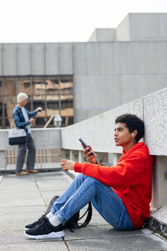 Diverse male friends sitting on rooftop checking smartphones with red hoodie and beanie, copy space