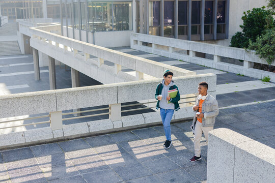 Diverse male students walking, chatting on campus with notebooks coffee and headphones, copy space