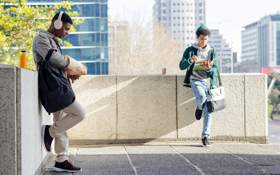 Standing on terrace, diverse male classmates opening paper bag, writing in notebook near coffee cup - Powered by Adobe