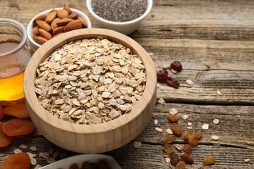 Making granola. Oat flakes in bowl, dried fruits, chia seeds, almond nuts and honey on wooden table, closeup. Space for text
