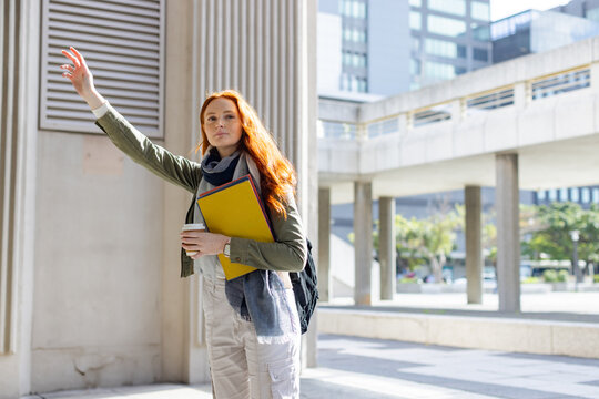 Woman raising arm holding coffee cup and yellow binder beside column in urban plaza, copy space