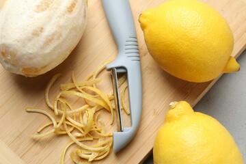 Fresh lemons with zest and peeler on grey table, closeup