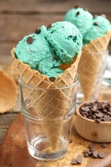 Tasty mint chocolate chip ice cream in waffle cones on wooden table, closeup