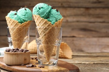 Tasty mint chocolate chip ice cream in waffle cones on wooden table, closeup. Space for text