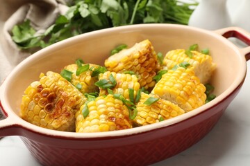 Pieces of grilled corn cobs with green onions on white table, closeup