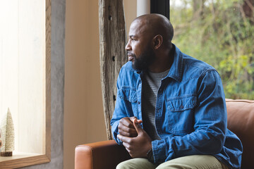 African American man sitting in living room on sofa by window with tree-shaped decorations