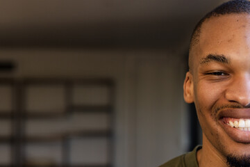 African American man smiling in green t-shirt at home workspace with wooden shelves, copy space