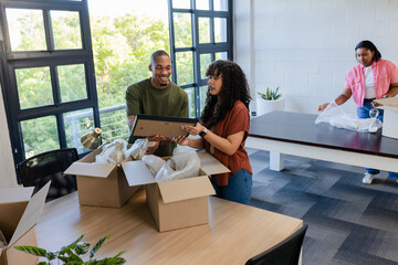 Diverse coworkers unpacking framed picture and bubble wrap at wooden tables in renovated office