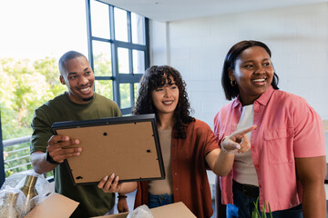 African American friends unpacking boxes, arranging picture frame, lamp, plant in living room