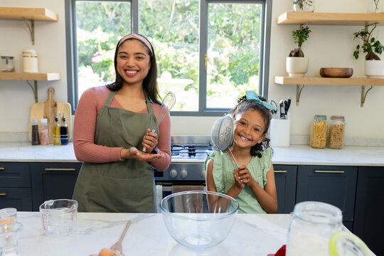 Mother and daughter with whisk and strainer whisking flour into bowl on countertop in home kitchen