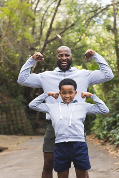 African American father and son in sportswear flexing biceps while smiling on paved woodland trail