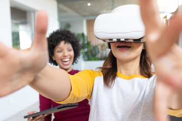 Diverse female coworkers exploring virtual reality using VR headset and tablet in open office space