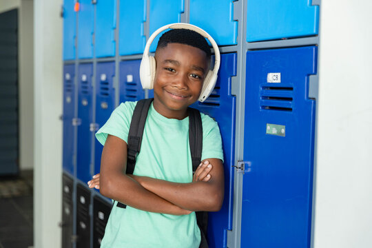 Teenage boy leaning against blue lockers in school hall, wearing mint tee, headphones, backpack