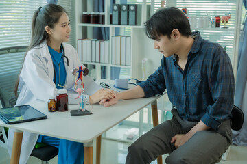 Fototapeta premium Asian female doctor discusses a model of the male urinary tract and conditions such as enlarged prostate, prostatitis, and cystitis.