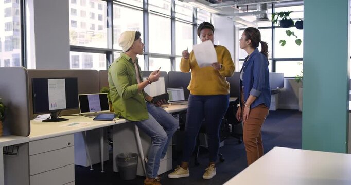 Diverse coworkers reacting to printed pages and planning next steps around workstation using tablet