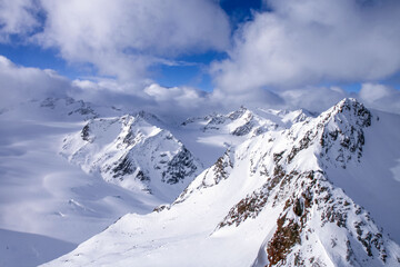 Fototapeta premium Majestic snow-capped Alpine mountains under a blue sky and clouds. Pure winter nature, impressive peaks and glaciers create an atmosphere of tranquility and grandeur.