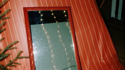 Dark Chirstmas Reflective surface on red wall with string lights and greenery.