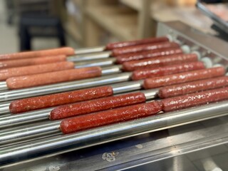 Long delicious hot dogs are sizzling on a roller grill in supermarket indoor, making them the perfect choice for outdoor gatherings and events. Close-up