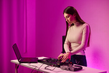 Female DJ mixing on turntables, colorful lighting studio, focused expression, hands adjusting mixer and laptop controls, wearing headphones, modern electronic music vibe, cinematic lighting
