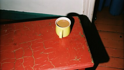 Dark Chirstmas A yellow cup of coffee on a textured red table surface.