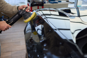 Polishing black car surface thoroughly, Detailed buffing to achieve showroom quality shine, Expert technician uses orbital buffer and foam pad to enhance vehicle gloss