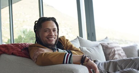 Mid adult man wearing bomber jacket sitting on sofa in living room smiling then laughing