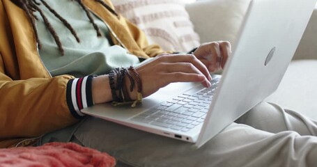 Middle-aged man opening silver laptop and typing for remote work on couch in living room - Powered by Adobe
