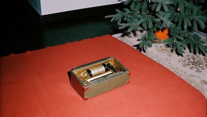 Dark Chirstmas Antique music box on a red rug beside a decorative tree.
