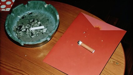 Dark Chirstmas Ashtray and envelope on a wooden table, cigarette butt present.