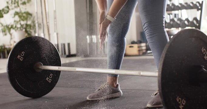 Hands clapping chalk over barbell on gym floor, chalk dust drifting while legs bracing for deadlift
