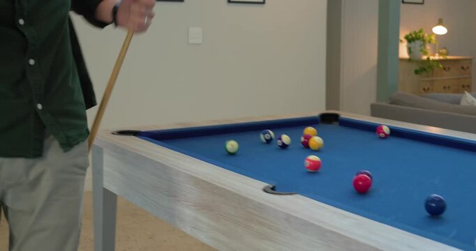 Mid adult man playing pool, breaking cue ball and scattering balls, planning shot in recreation room