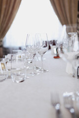 Festive table setting. Concept of holiday. Glasses of wine on table. White plates. VIP lounge in restaurant. White tablecloth. Place for advertising. Out of focus. Part of interior.