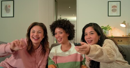 Diverse female friends reacting to TV at home, pressing remote grabbing popcorn, laughing