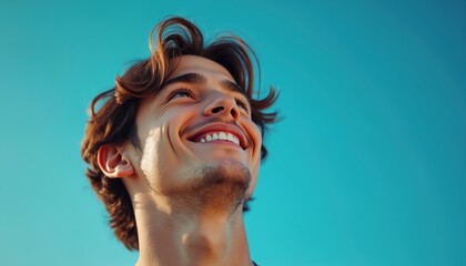 Smiling young man looks up at clear blue sky. He feels happy and hopeful, anticipating future plans. His expression is positive and optimistic, full of youthful joy.