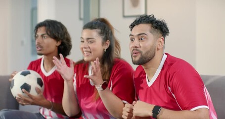 Friends wearing red jerseys on couch reacting to tense match gripping soccer ball before slumping