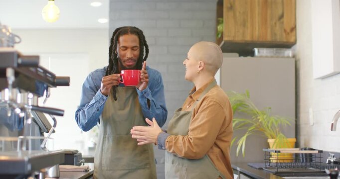 Diverse coworkers tasting brew behind counter, handing red mug, stirring with stick, inhaling aroma