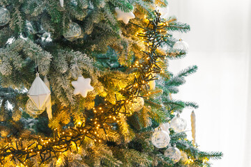 Snowy frosted Christmas tree branches decorated with white ornaments, warm glowing string garland lights, illumination on background. Soft winter atmosphere for holiday backdrop and seasonal designs
