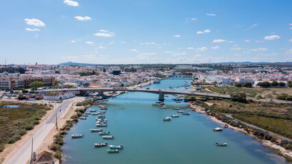Fototapeta premium Aerial view captures Tavira in Algarve with boats on the river Gilao a bridge connecting sides, and buildings in the background under a clear sky